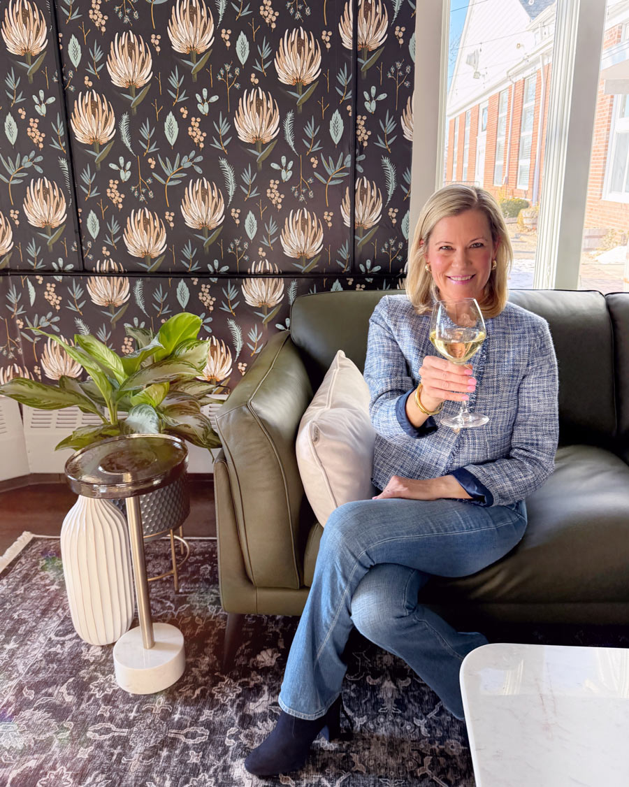 Courtney-Doyle-Holding-Glass-of-wine-in-front-of-floral-print-background-next-to-plant